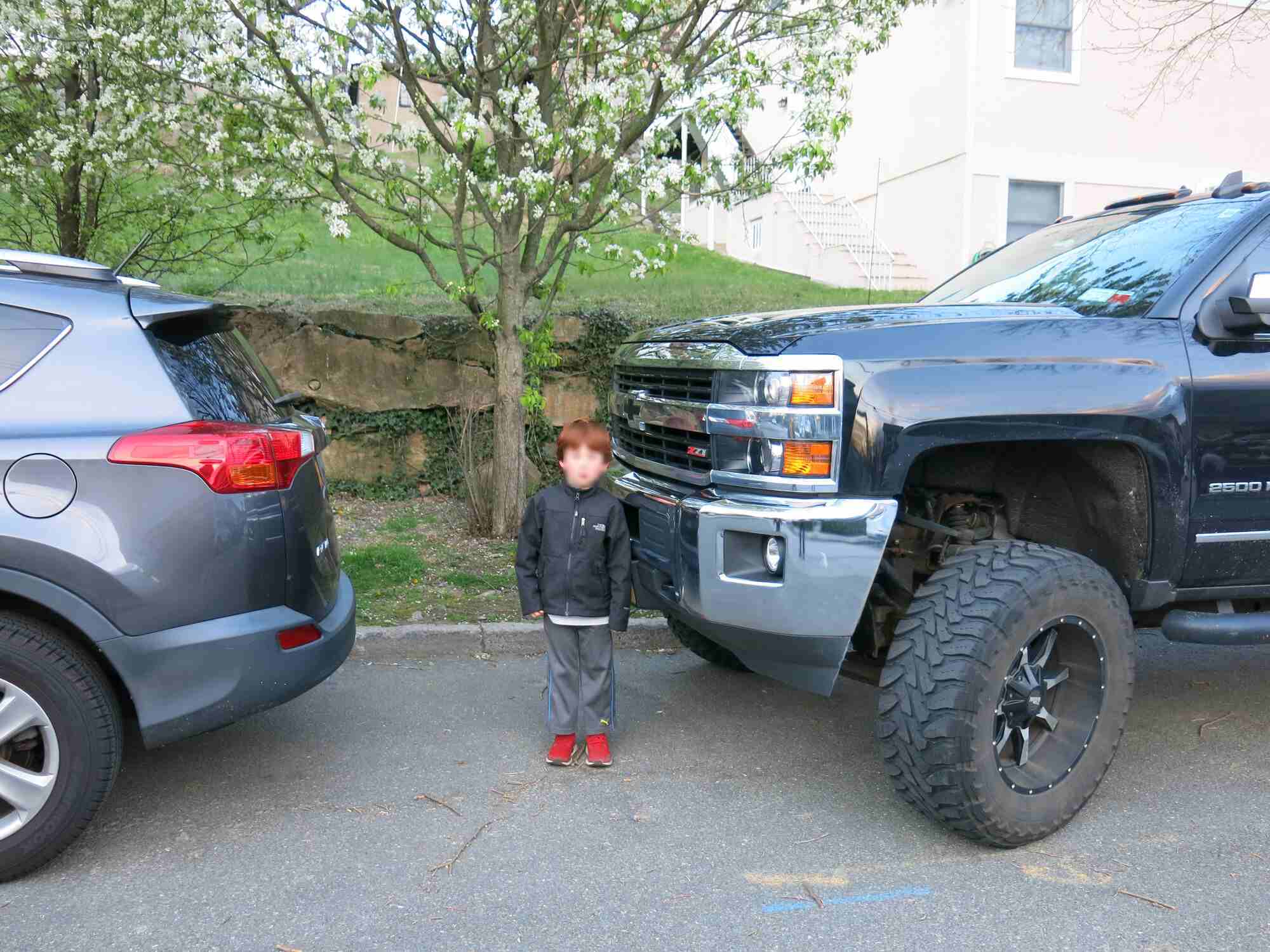 A kid standing in front (and dwarfed by) of a Chevy Silverado 2500 pickup truck with lift kit.